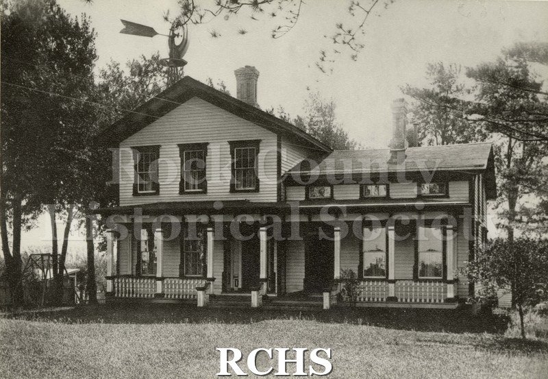 Black and white photograph of Schmidley Homestead house with trees, windmill, glider and smaller building in background.