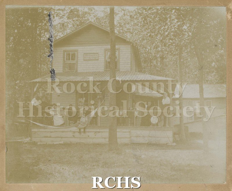 Black and white photograph of Tallman's Hickory Lodge. Very faded. Two story house with wrap-around porch. One story to right of house.