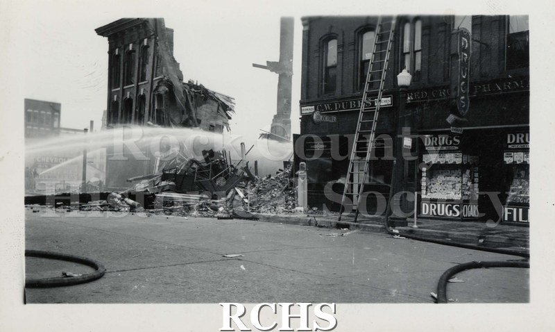Black and white photograph of Milwaukee Street Bridge fire, 1941. From left side of photograph, a stream of water to space between two buildings.