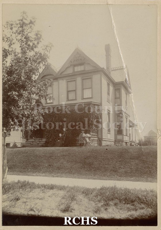Black and white photograph of 811 Nicollet Ave.,/ Minneapolis, MI. Shows a young girl with a doll and stroller outside a house as well as two women. .