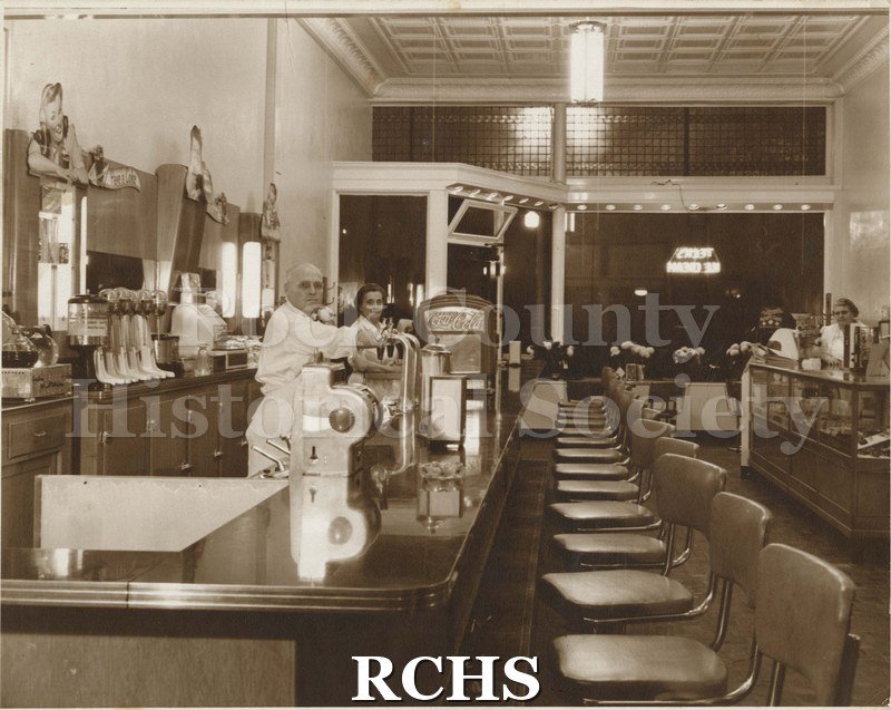 Black and white photograph of a man and woman behind the counter of a Teck's Ice Cream parlor. There is another woman at the counter on the right.