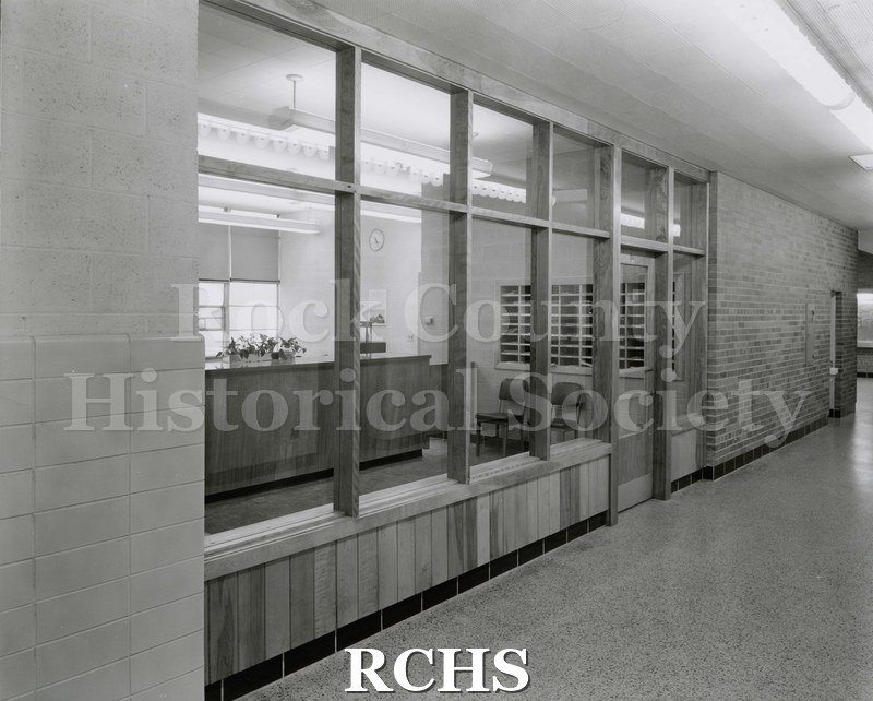 Black and white photograph of the interior of Janesville Senior High School, looking into the office area.