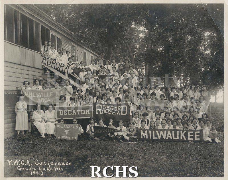 Black and white photograph of many young women sitting and standing in front of building.