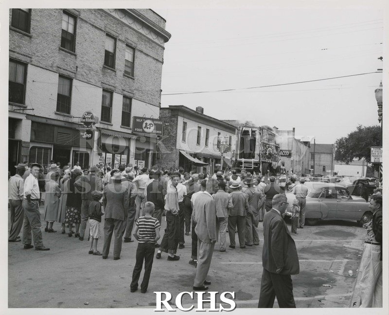 Black and white photograph of people standing in the street waiting for the parade to start.