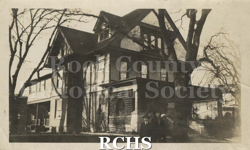 Black and white photograph of of 227 N. Washington St., Janesville, WI. Shows a three story house with a porch. There are trees in front of the house.