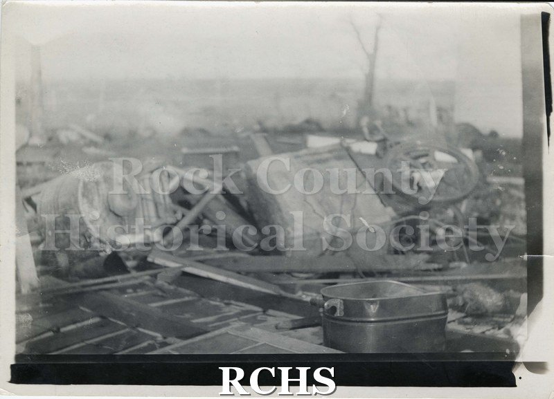Black and white photograph of tornado 1911. Shows a building demolished in the tornado. There is a roaster pan sitting on the ground in front of the debris.