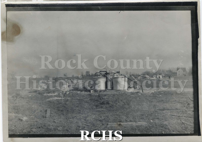 Black and white photograph of the tornado in Rock County 1911. Shows gas tanks which have been damaged by a tornado.