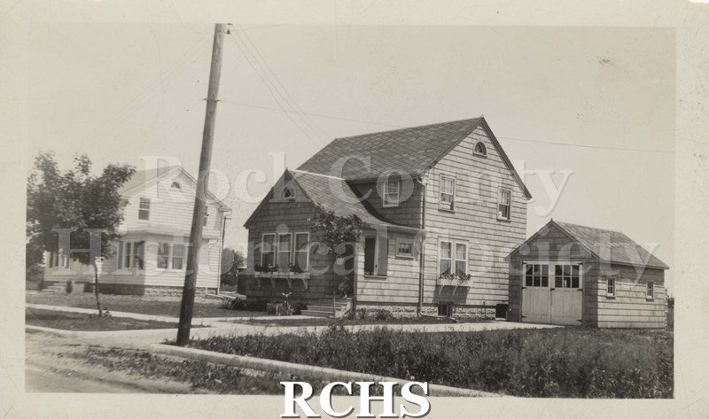 Black and white photograph of Chester Welch Residence. This is a two story house with a garage on the side. There is another residence visible on the left.