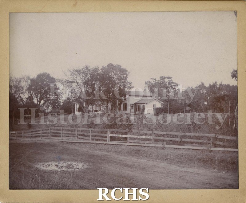 Black and white photograph of Miltimones Home 1868. Shows a house set back from the road with a fence in front of it.
