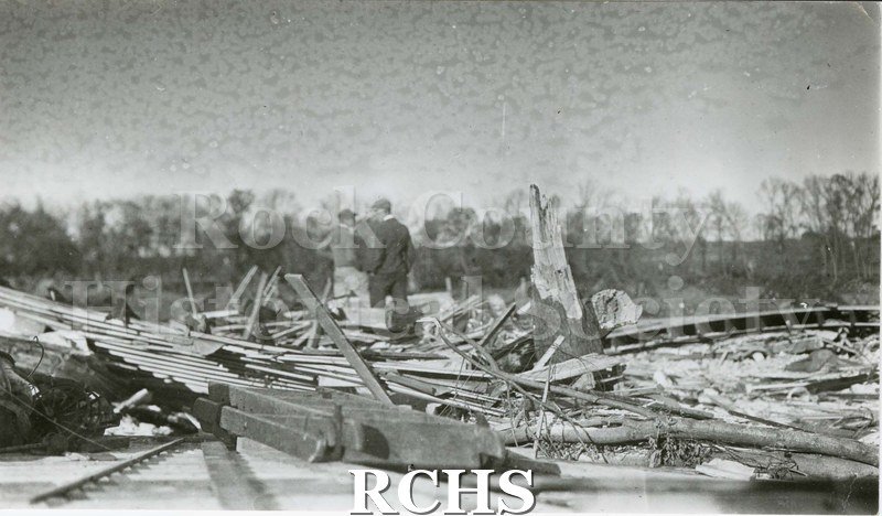 Black and white photograph of two men standing in the debis of a building damaged by the tornado of 1911.