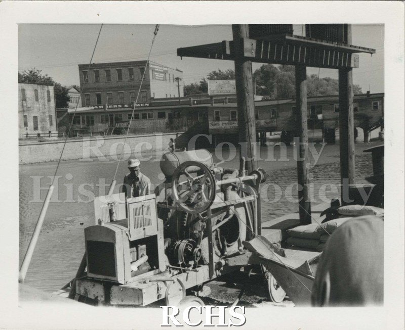 Black and white photograph of workman using a machine to clear debris from the fire.