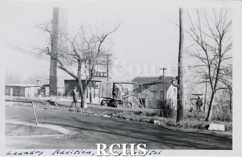 Black and white photograph of Mercy Hospital Laundry Addition under construciton. Shown is a crane parked in front of a building.