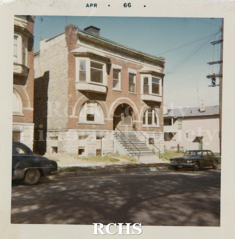 Color photo of Jeffris Flats, a two story brick apartment building with basement apartments and steps leading up to an arched doorway.