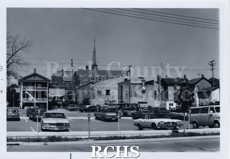 Black and white photograph of Main St., North Parking lot with cars parked and the backs of buildings in the background.