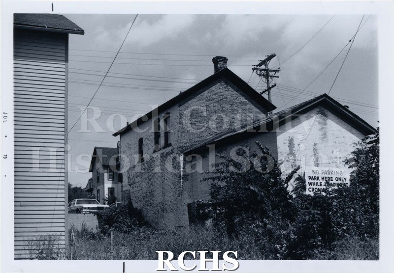 Black and white photograph of the back of a brick building on Parker Drive. There is a sign for No Parking.