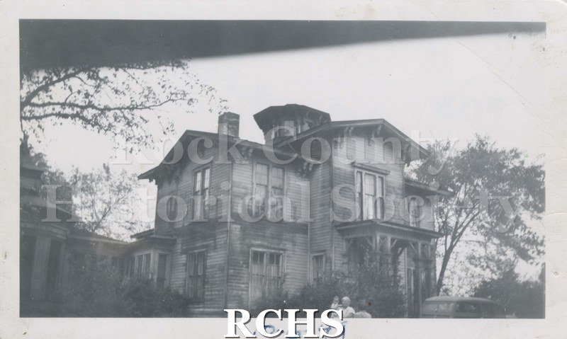 Black and white photograph of J. B. Crosby House. Shows a two story house set among trees. There are people visible at the bottom of the photo.