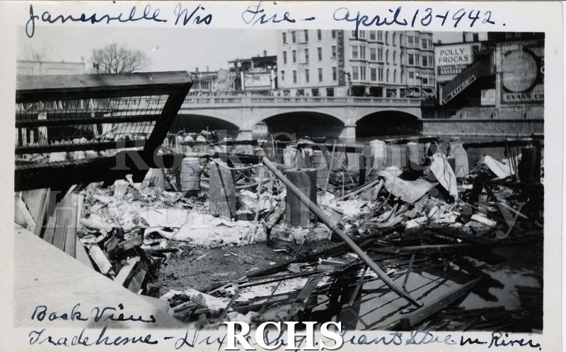 Black and white photograph of Janesville Wis.Fire April 13, 1942. Shows debris in front of the bridge and sign: "Polly Frocks" on the right side.