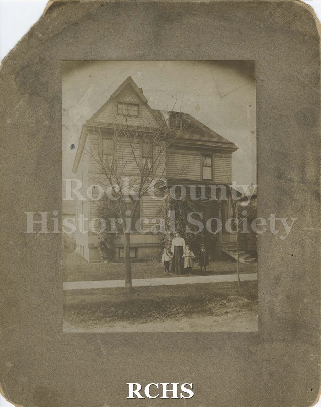 Black and white photograph of three story house at 106 Linn Street, Janesville, WI, with a woman and three children standing in front of it.