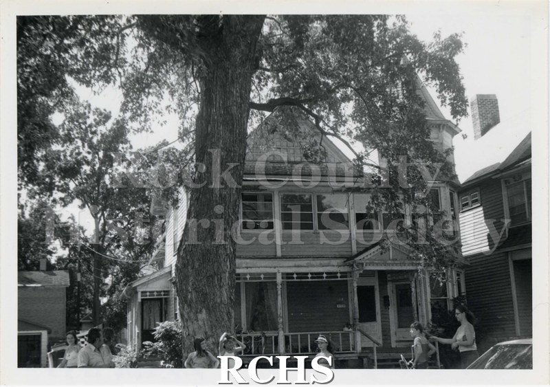 Black and white photograph of 108 Cherry Street, a three story building with a porch on the front. There are people standing in front of the building.