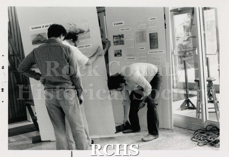 Black and white photograph of three people working on an exhibit.