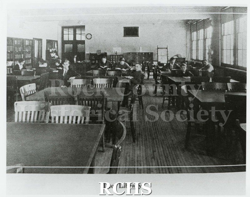 Black and white photograph of the Janesville High School library with students seated at library tables. Caption on photo: "The Library".