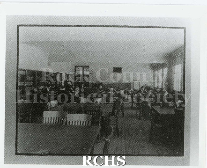 Black and white photograph of the Janesville High School library. Students seated at library tables. Written on reverse: "Library 1924 Phoenix pg. 18".