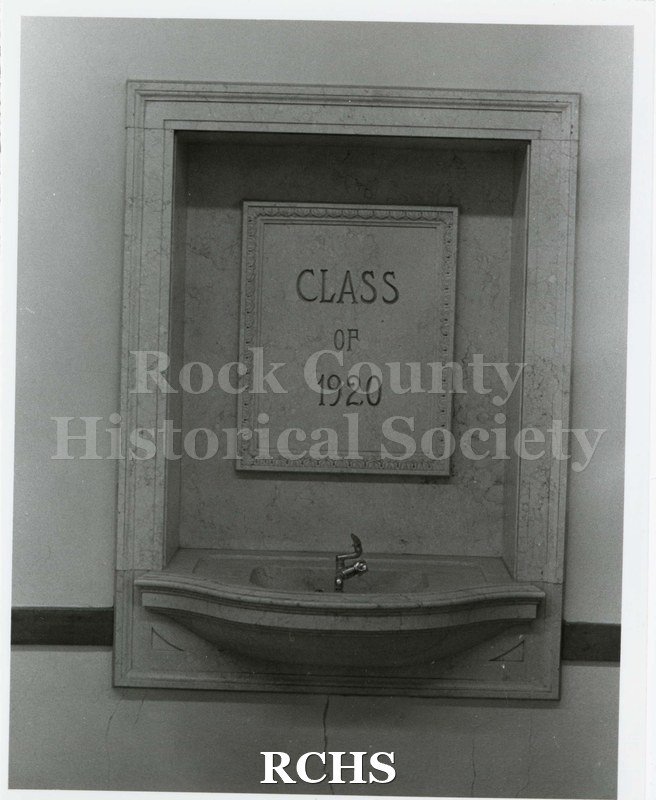 Black and white photograph of the drinking fountain at Janesville High School with memorial plaque above stating "CLASS OF 1920".