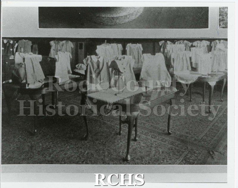 Black and white photograph of dining room tables with clothing displayed on them. Written on reverse: "Model Dining Room 1927 Phoenix pg.72".