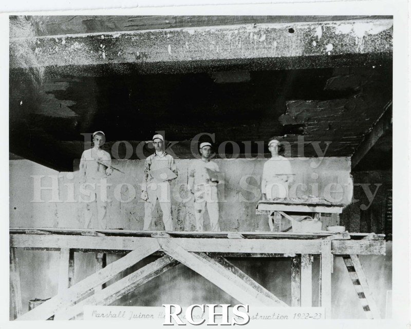 Black and white photograph of four men on scaffolding. Appear to be plastering. Written on reverse: "Auditorium 1922-3".