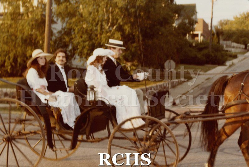 Colored photograph of the Janesville Public Library Centennial Exhibit .Shows two couples seated in an open carriage pulled by one horse.