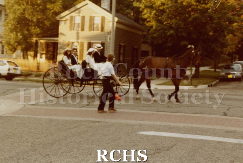 Colored photograph of the Janesville Public Library Centennial Gala. Shows two couples seated in an open carriage pulled by one horse.