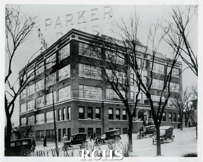 Black and white photograph of the Parker Pen Company headquarters building circa1920. Five automobiles parked on street alongside building.