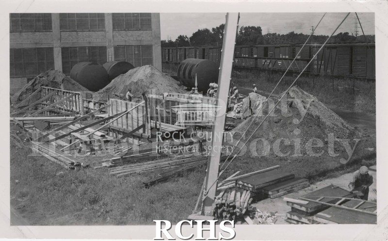 Black and white photograph of an unidentified construction site (Chevrolet?). Shows men working on putting up walls.