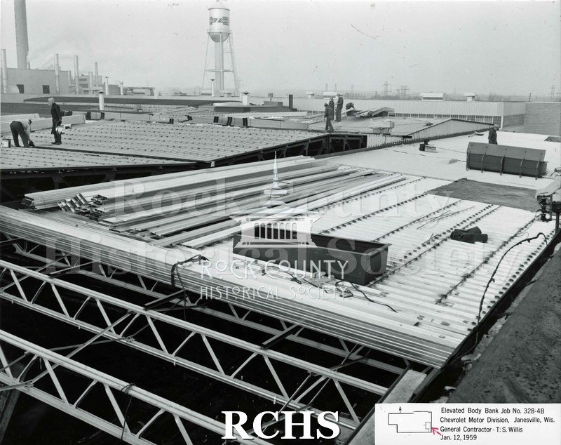 Black and white photograph of the roof of the Chevrolet building. There are several construction workers walking around on the roof.