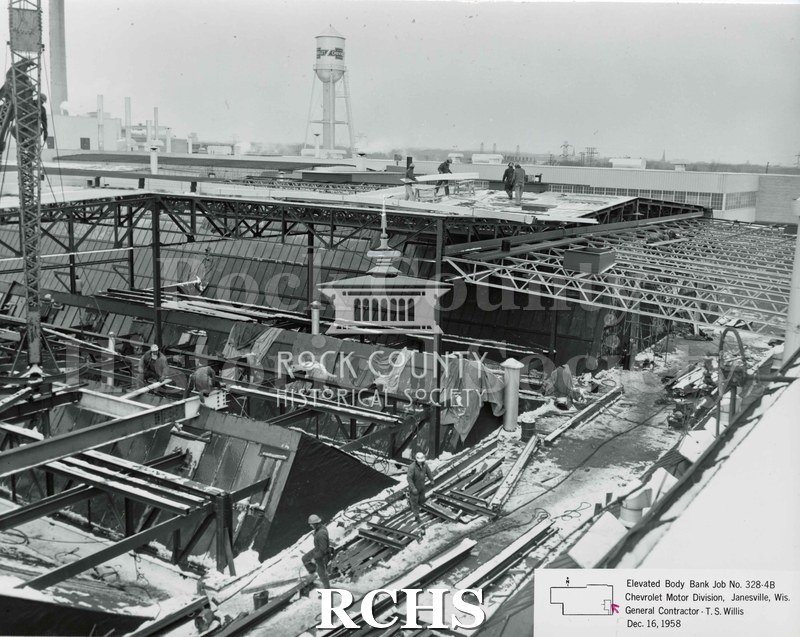 Black and white photograph of the roof and sides of the Chevrolet building. There are construction workers in the foreground and on the roof.