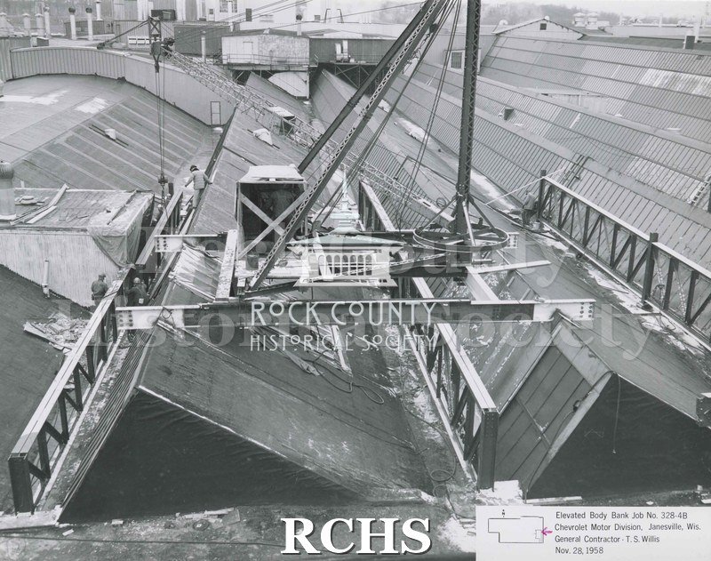 Black and white photograph of the roof and girders on the Chevrolet plant addition. There is snow on the panels. Two construction workers are shown on the left side.