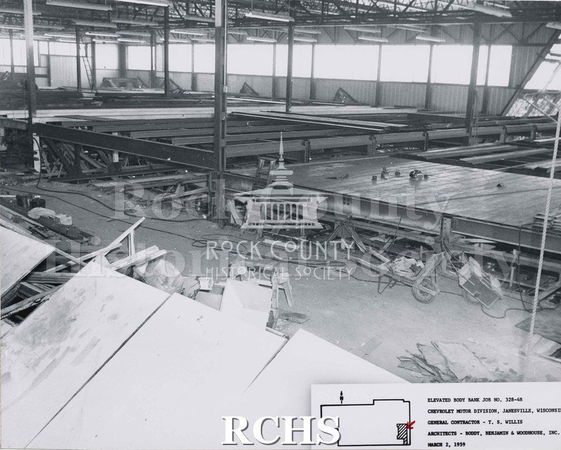 Black and white photograph of the inside of the Chevrolet factory. Shown are various pieces of construction equipment, such as a sawhorse, a wheeled cart, and.