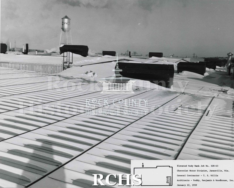 Black and white photograph of the roof of the Chevrolet building covered with snow. There is a water tower visible in the background.