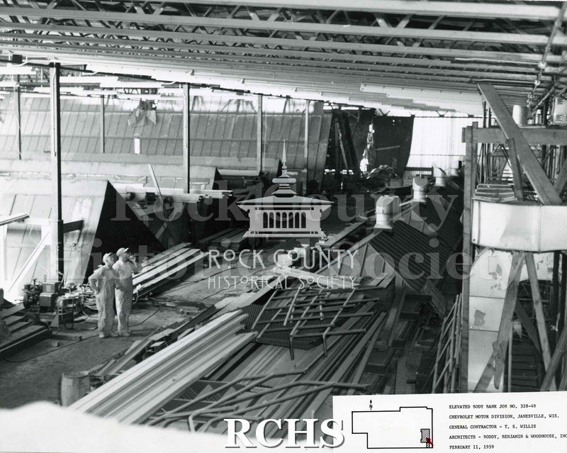 Black and white photograph of the inside of the Chevrolet building. Two construction workers on the left side are looking up. On bottom: "Elevated Body Bank Job No.