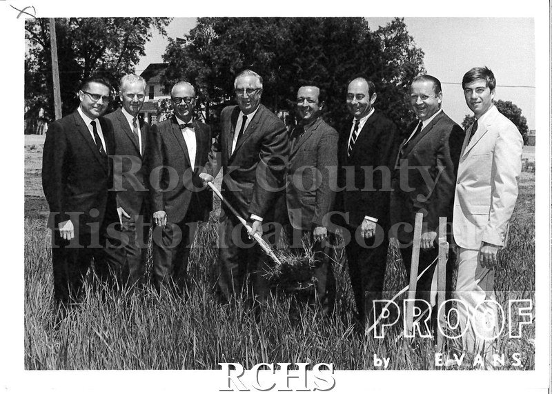 Black and white photograph of the Rock County Buick Co. Groundbreaking Ceremony. Shows 8 men at a groundbreaking ceremony. The man in the middle is holding a shovel.