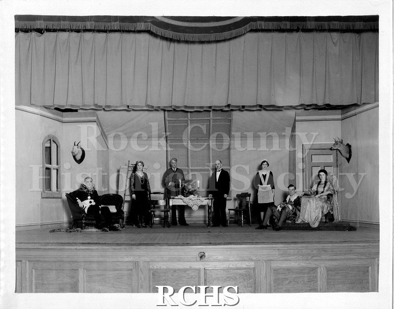 Black and white photograph of seven actors for an unidentified play. They are posed onstage in a set of an interior room.