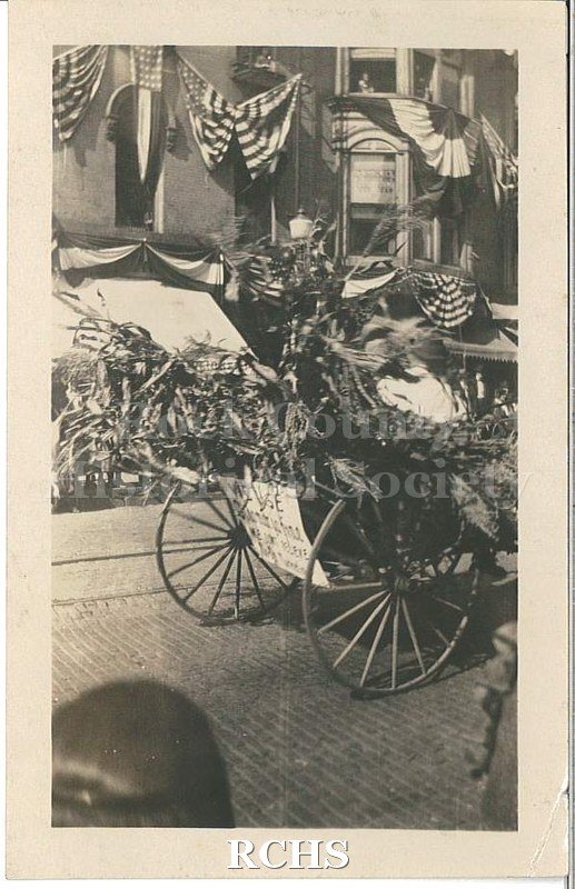 Black and white photograph of Harvest Festival Sept. 22, 1922. Shows a carriage decorated with corn stalks driving down a brick street.