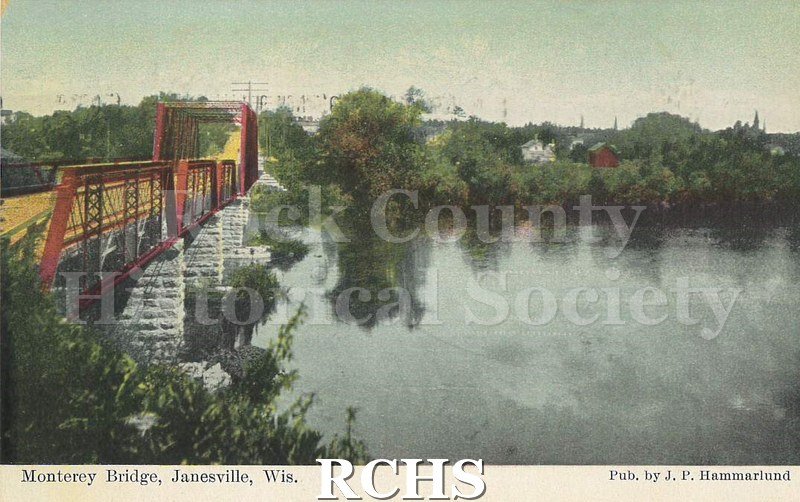 Postcard. Colored image of the Monterey Bridge in Janesville. The bridge is to the left of the image, and features a wood plank board and red steel frame.