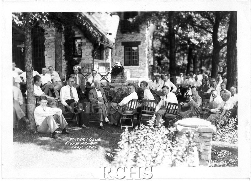 Black and white photograph of several men sitting on chairs on the lawn in front of a house. On bottom, in white: "Rotary Club Stone Henge July 1930 Rex".