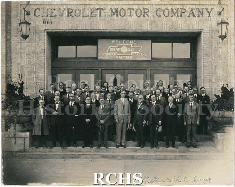 Black and white photograph of several men standing in front of the Chevrolet Motor Company. On front, in blue ink on bottom right: "Return to R. C.