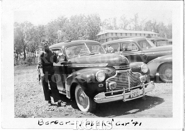 Black and white photograph of WWII Training Fort Knox, KY. Man standing outside next to a car. The man is wearing WWII military uniform with his sleeves rolled up.