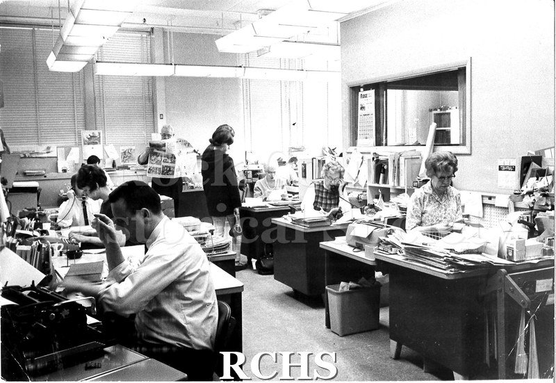 Black and white photograph of the Janesville Gazette offices, showing staff working at their desks. Eleven people are visible in the photo.