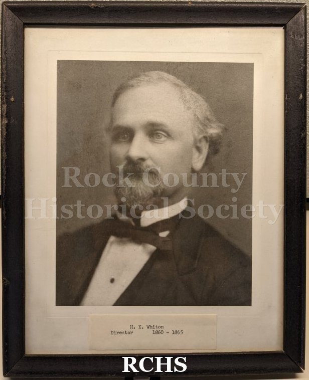 Black and white studio portrait bust of an old man in a suit, mounted behind glass in a black wood frame.