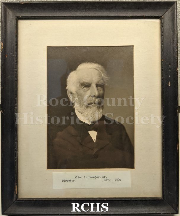 Black and white studio portrait bust of an old man in a suit, behind glass in a black frame.