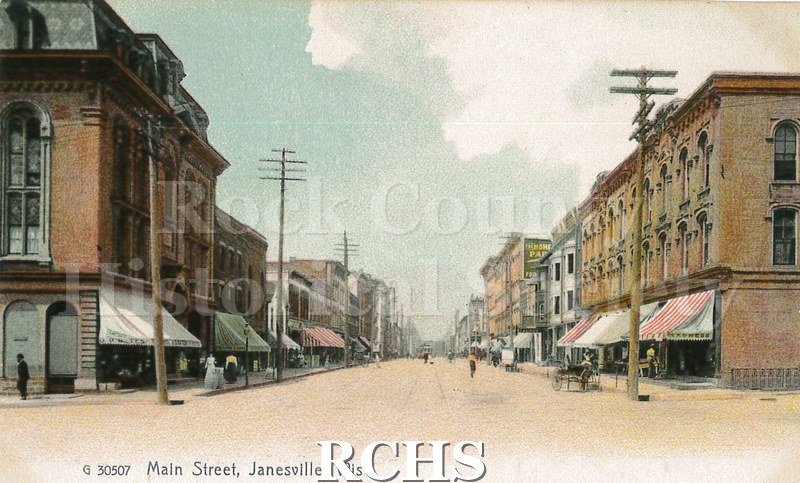 Postcard. Colorized image of Main Street in Janesville, Wisconsin. Postcard is not addressed, but has a brief note on the back in pencil. "Janesville, Wis.